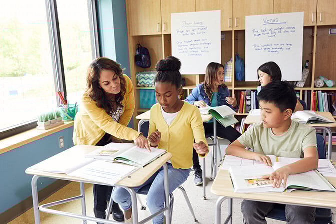 Four students at desks work with teacher. Four students at desks work with teacher.
