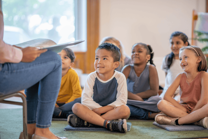 Teacher reading aloud to students sitting on the floor of the classroom